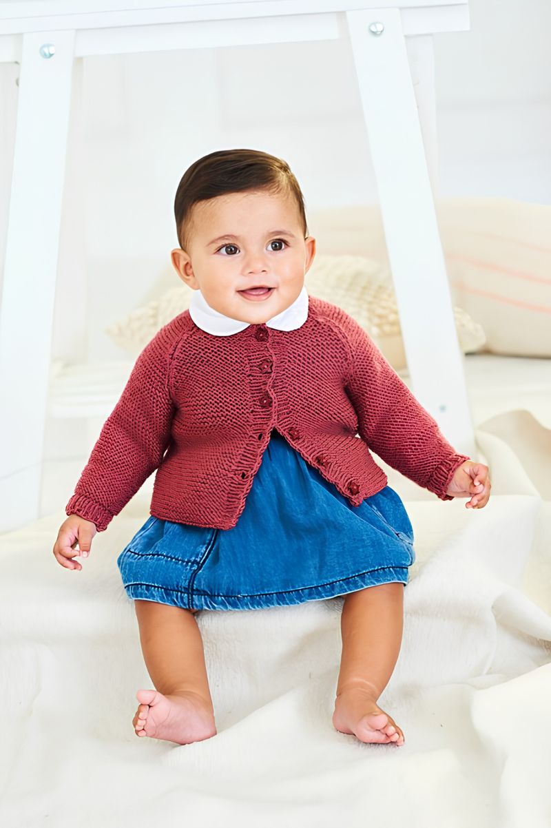 Baby wearing a red knitted cardigan and blue skirt on a white background