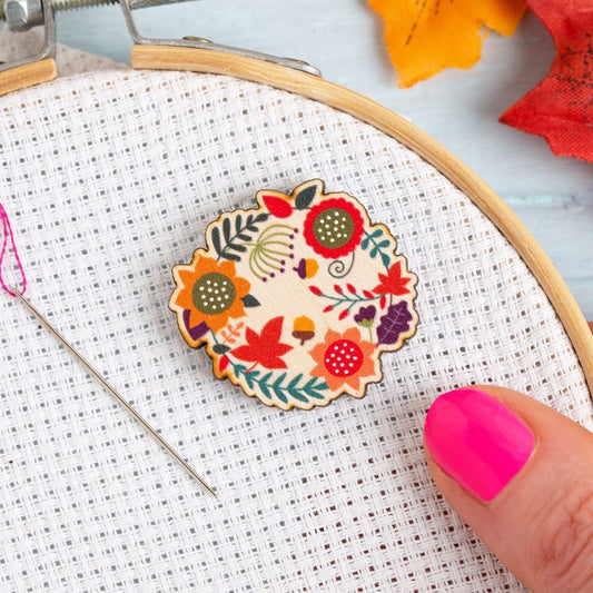 Hawthorn Handmade Autumn Leaves magnetic needle minder on Aida fabric in embroidery hoop, with an embroidery needle next to it.