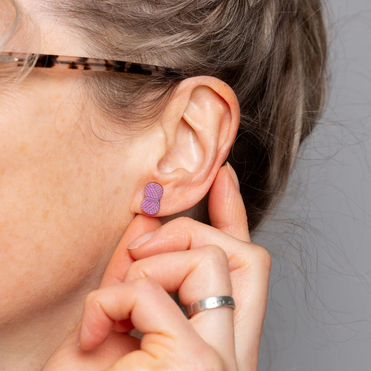 Close-up of a person wearing a mauve yarn ball earring.