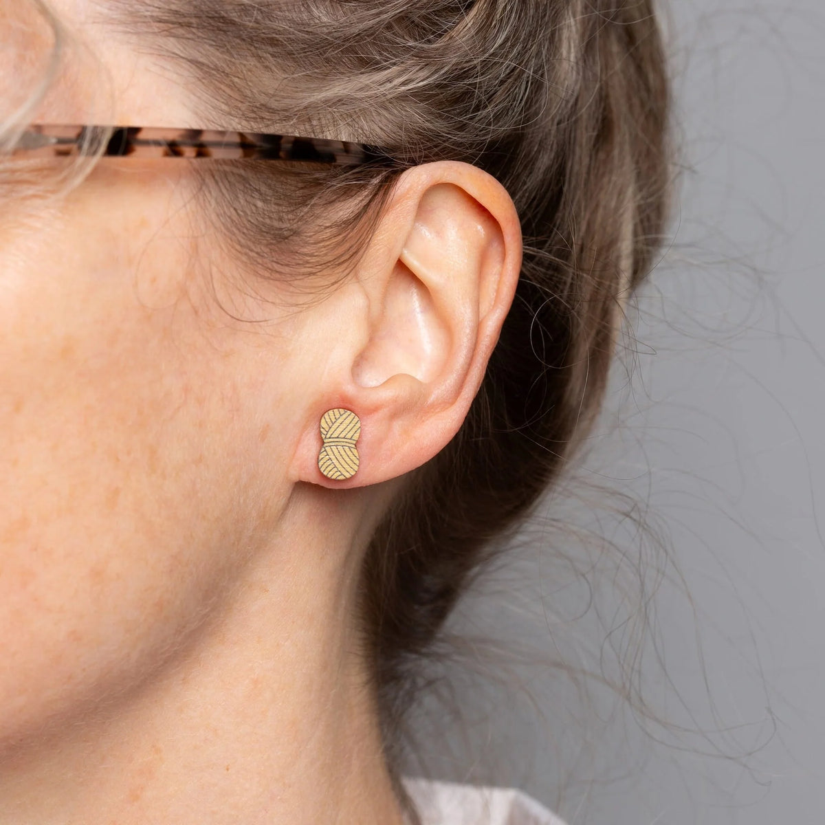 Close-up of a person wearing Mustard yarn shaped earrings against a neutral background.