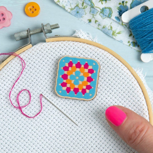Embroidery hoop with a Hawthorn Handmade granny square magnetic needle minder , thread, and needle on a light blue background.