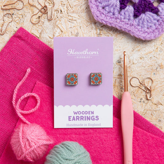 Wooden granny square earrings on a Hawthorn & Co card with knitting materials in the background.