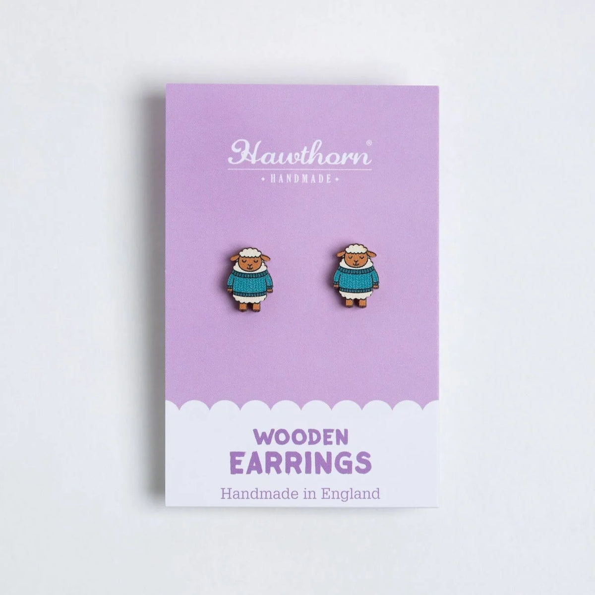 A pair of small wooden sheep stud earrings displayed on a lavender card labeled Hawthorn Handmade, against a clean white background.
