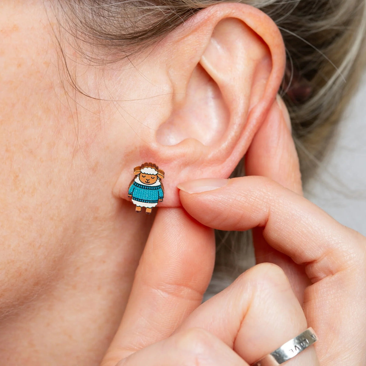 Person wearing a woolly sheep stud earring with a hand adjusting it.