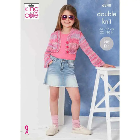 King Cole easy knit dk pattern featuring a young girl wearing a pink knitted cardigan and denim skirt, standing next to a white stool.The pattern is 6348.