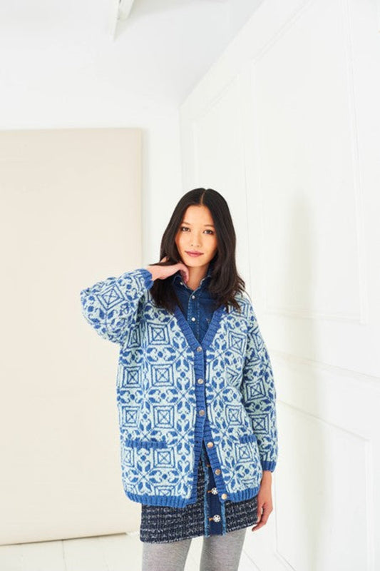 A model wearing a colourwork cardigan knitted in Stylecraft Life DK yarn, using shades Denim and Mint Wash. It features a geometric blue pattern on a white background with blue cuffs and seams. The cardigan is from Stylecraft pattern 10283.